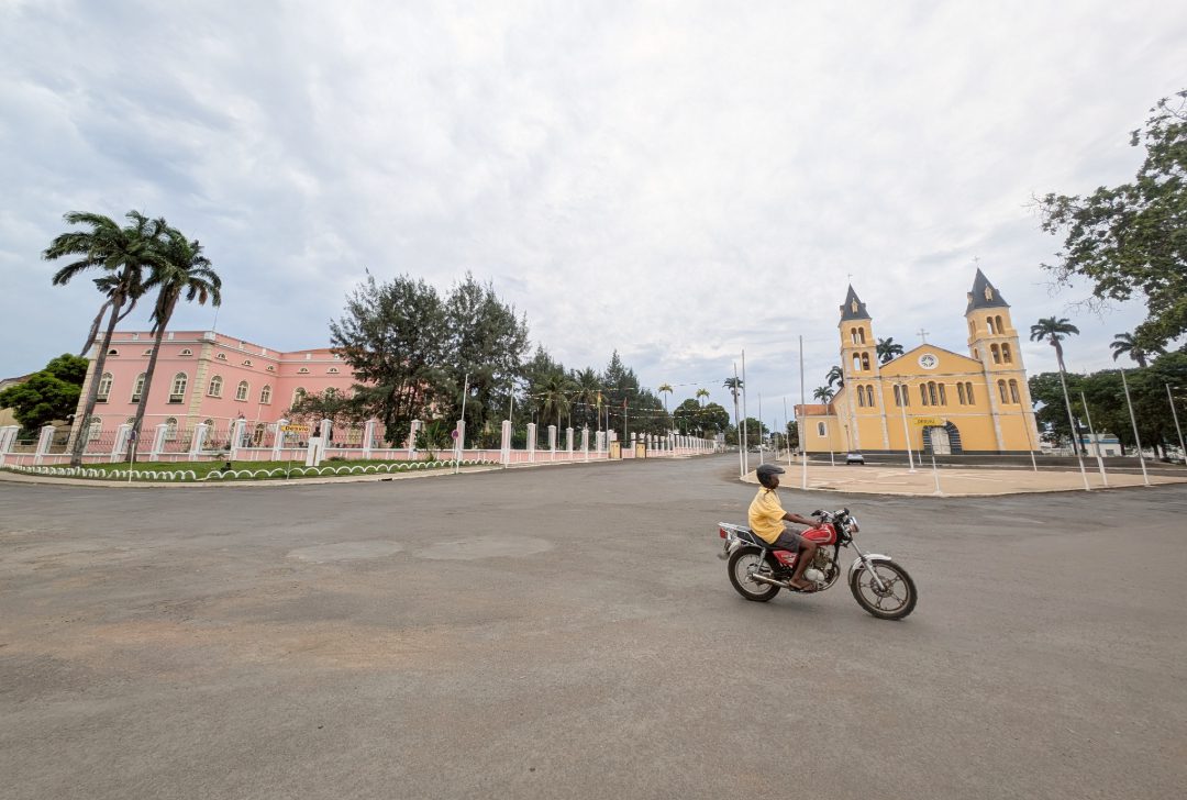 Rosafarbener Palast und gelbe Kirche in einer leeren Stadt, davor ein Moped