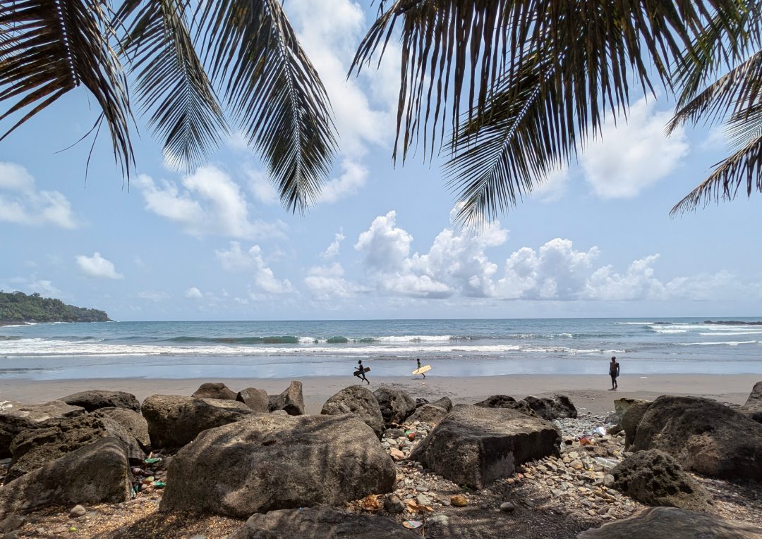 Dunkler Sandstrand, auf denen Surfer mit Holzbrettern unterwegs sind