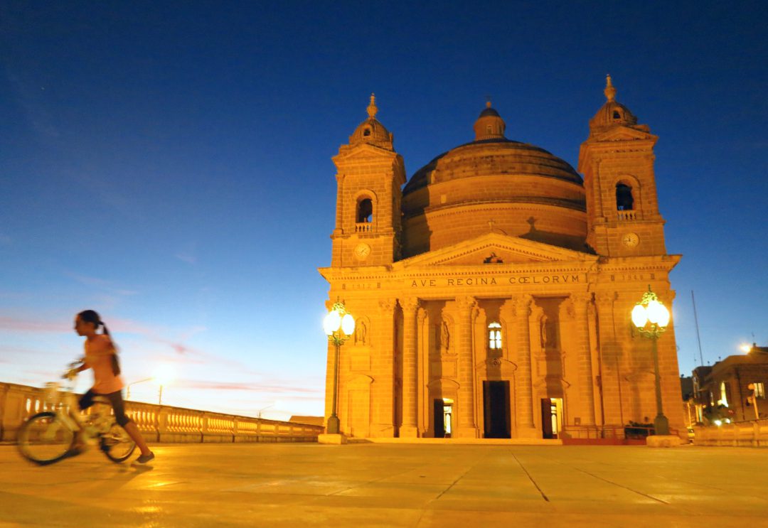 Kirche in nächtlicher Beleuchtung, davor ein Kind mit Fahrrad